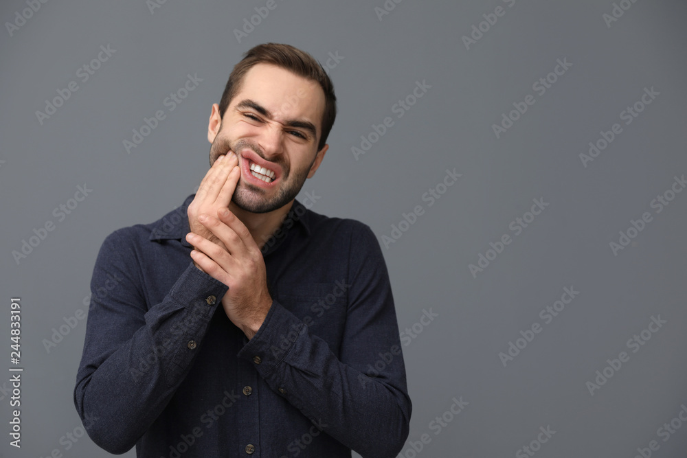 Young man suffering from strong tooth pain on grey background, space for text Young man suffering from strong tooth pain on grey background, space for text