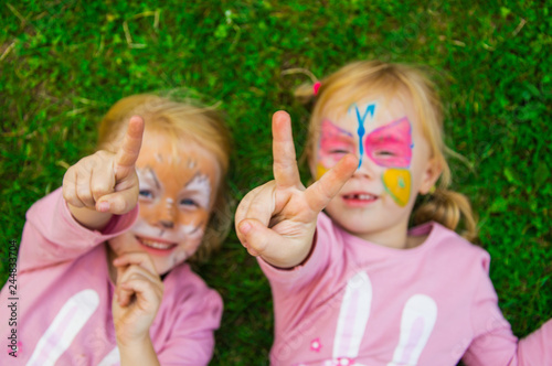 two little girls with colorful painted faces having fun on the grass