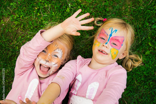 two little girls with colorful painted faces having fun on the grass