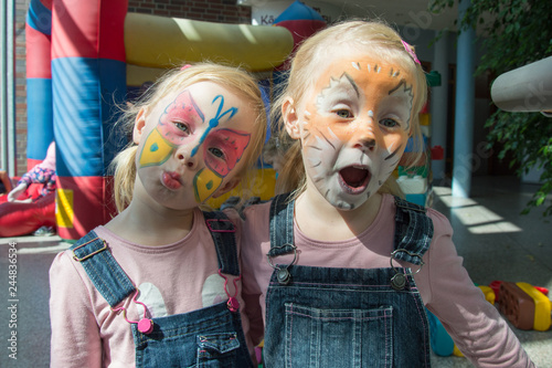 two little girls with brightly decorated faces of a butterfly and a lion cub, having fun at a children's party