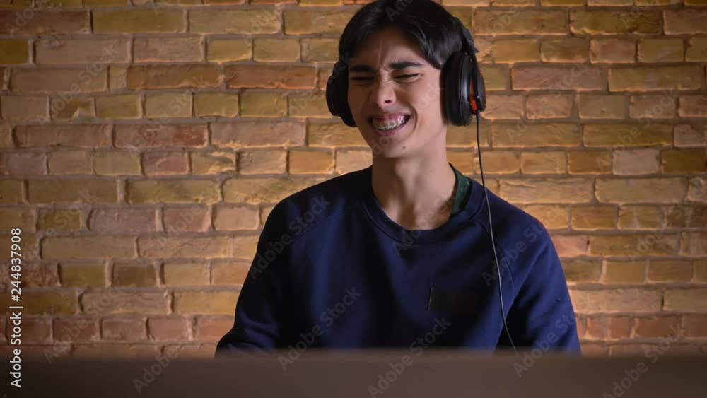 Closeup portrait of young attractive korean man in headphones playing video games and failing the level indoors Closeup portrait of young attractive korean man in headphones playing video games and failing the level indoors