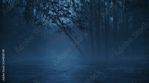 Moody blue mist and fog shroud a flooding river overflowing its banks at dusk