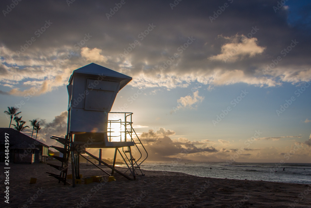 A Tropical Beach Lifeguard Station at Sunrise - with a Partially Obscured Sun and Palm Trees and Heavy Clouds in the Background