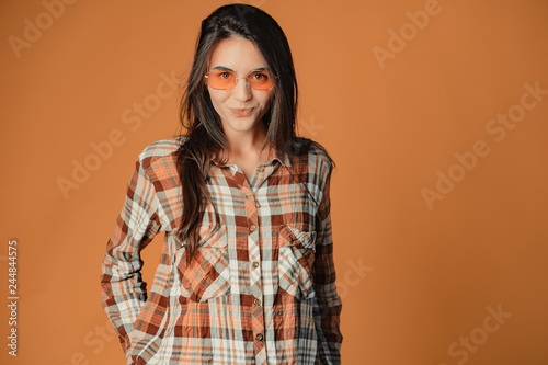 Cute playful young brunette girl making faces on orange background