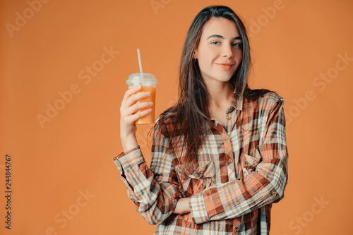 Cute caucasian young brunette girl holding orange juice on orange background