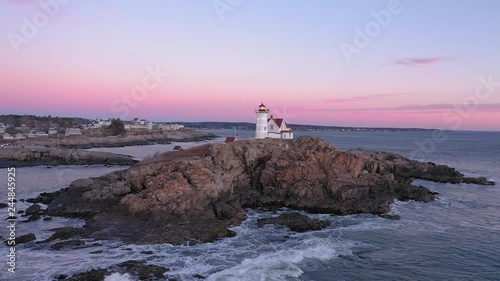 Aerial ORBIT to right around Nubble Lighthouse in Maine just before a cold December sunrise revealing beach houses and a full moon photo