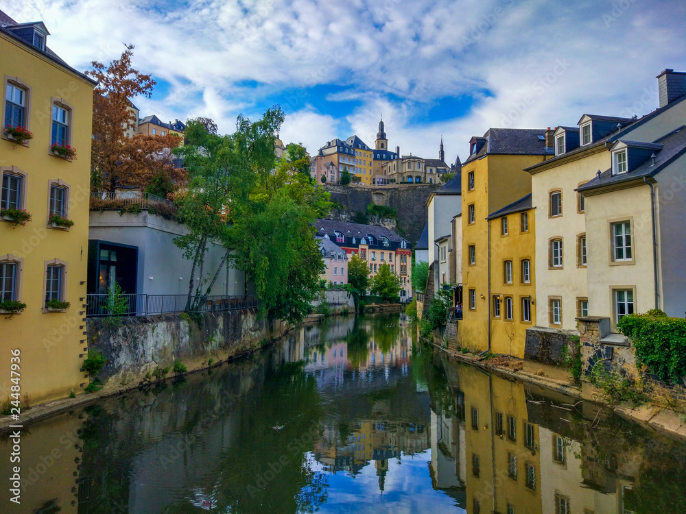 Colorful houses in the Alzette river in old town (Grund district) of Luxembourg, with beautiful reflections in the water and Saint Michael's Church (Eglise Saint-Michel) at the top