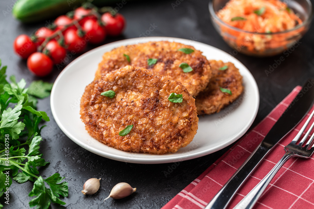 Cutlets lie on a white plate. Chicken cutlets lie among the vegetables on a black stone table.