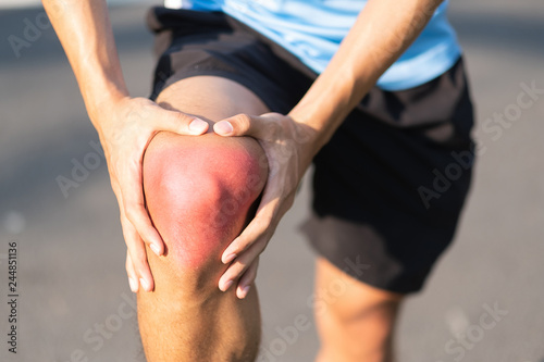 Young fitness man holding his sports leg injury. muscle painful during training. Asian runner having knee ache and problem after running and exercise outside morning. sport and healthy concepts