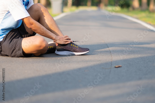 Young fitness man holding his sports leg injury. muscle painful during training. Asian runner having ankle ache and problem after running and exercise outside morning. sport and healthy concepts