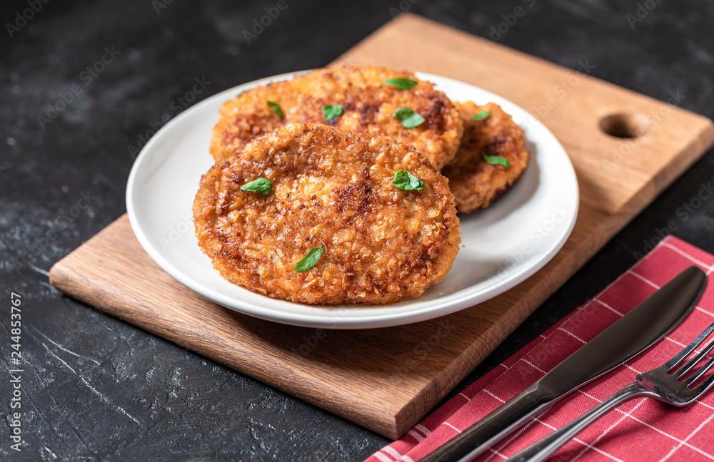 Cutlets lie on a white plate. Chicken cutlets lie among the vegetables on a black stone table. Cutlets lie on a white plate. Chicken cutlets lie among the vegetables on a black stone table.