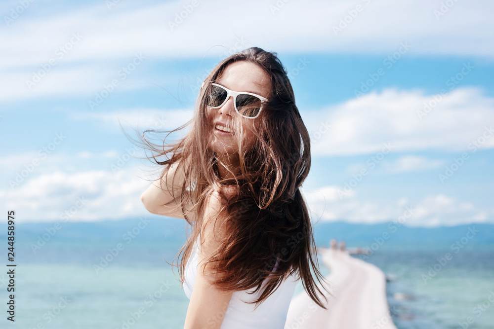Young beautiful stylish woman brunette girl with flowing hair in sunglasses is not the shore of the blue tropical sea Young beautiful stylish woman brunette girl with flowing hair in sunglasses is not the shore of the blue tropical sea