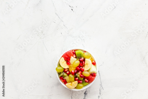 Fruit diet concept. Fruit salad with apple, kiwi and pomegranate in bowl on white stone background top view copy space