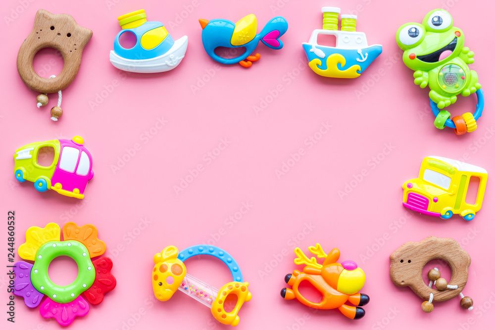 Handmade toys for newborn babies, plastic and wooden rattle on pink background top view copy space frame