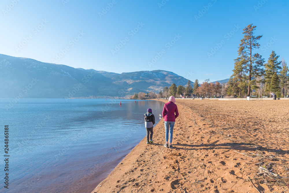 Girl and boy walking along sandy beach on sunny day with blue sky in winter
