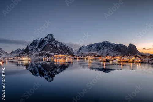 Fishing village illumination with mountain range  reflection on coastline at dawn photo