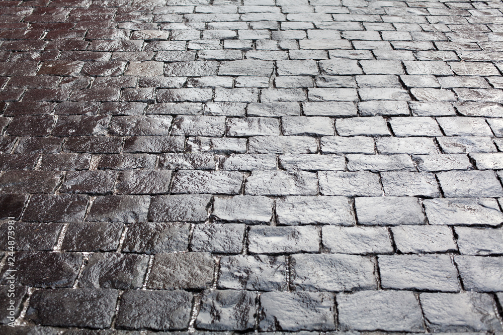 Cobblestones on pavement background, stone sidewalk texture gray or black color, wet bricks road surface pattern top view closeup