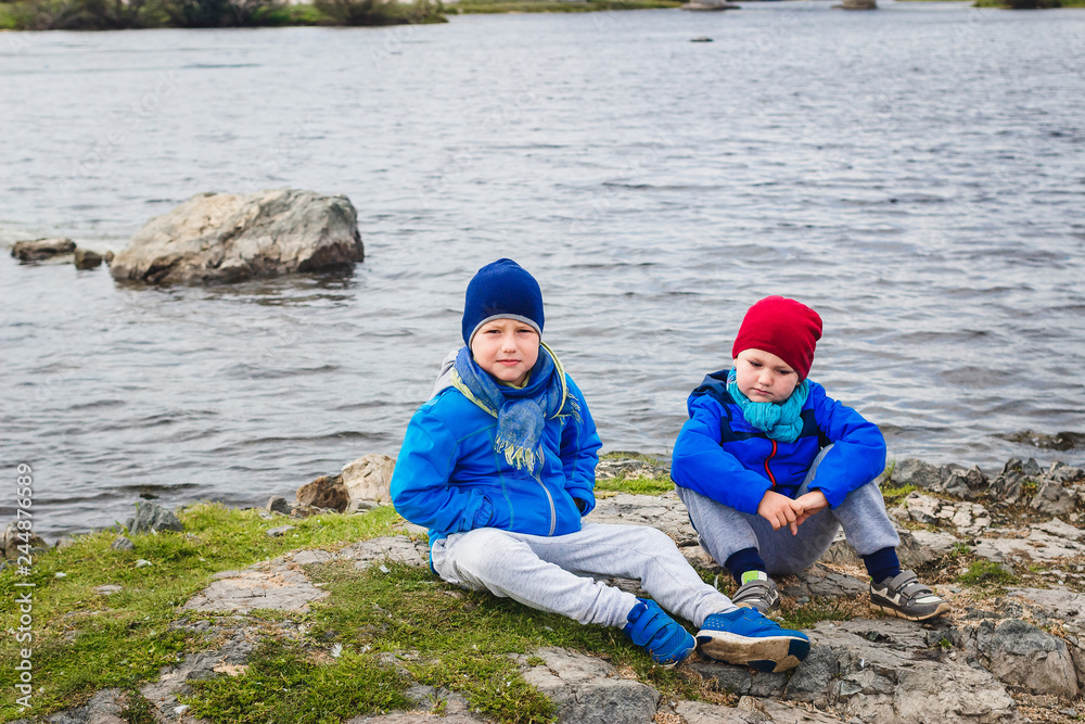 two boys sit on the banks of the River in the spring