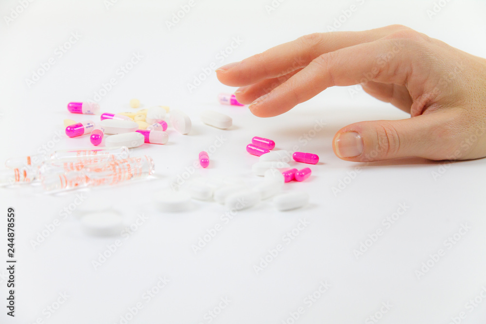 Addiction to medicines and drugs in modern times: close-up shot of a young woman's hand about to grab various tablets and vials on table and white background Addiction to medicines and drugs in modern times: close-up shot of a young woman's hand about to grab various tablets and vials on table and white background