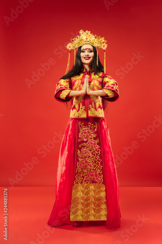 Chinese traditional graceful woman at studio over red background. Beautiful girl wearing national costume. Chinese New Year, elegance, grace, performer, performance, dance, actress, dress concept