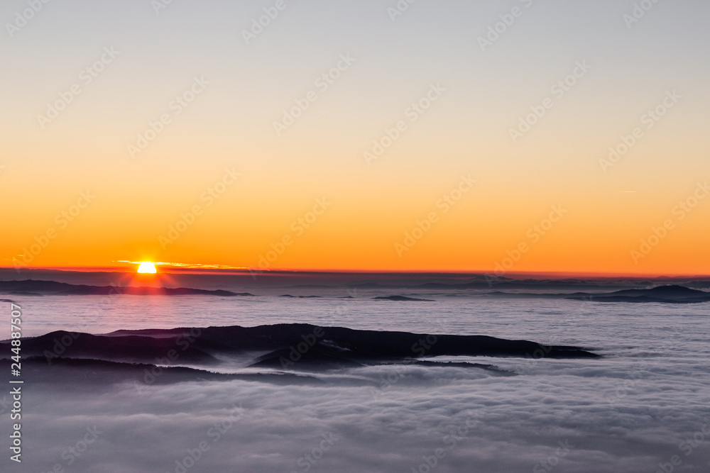 Fototapeta premium Beautiful sunset over a valley filled by fog with mountains and hills