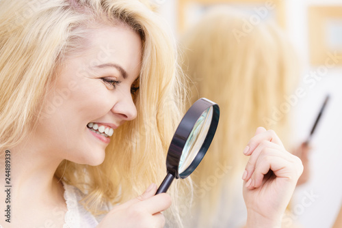 Happy woman looking through magnifer at hair photo