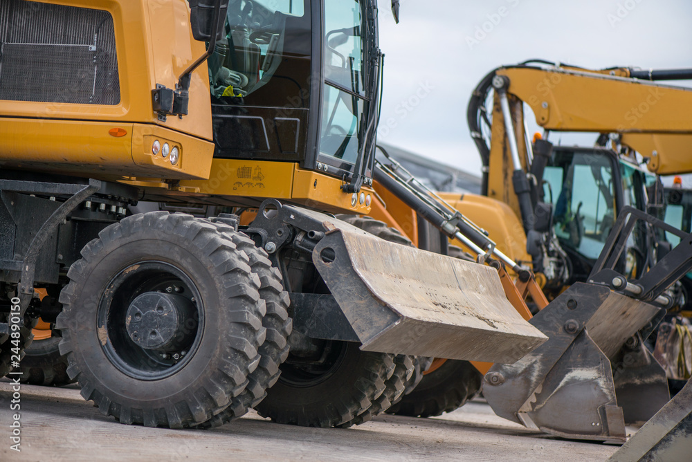 Multiple cars, excavators, trucks, loaders, concrete mixers and construction machinery in large parking lot in industrial territory, next to concrete and asphalt factory  