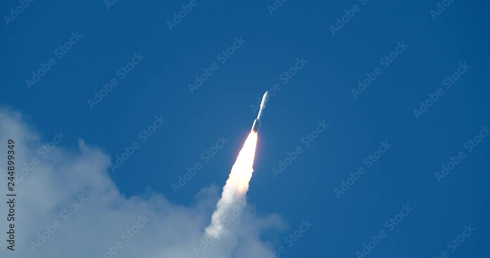 Rare shot of commercial Space Rocket with bright flames and exhaust smoke emerging from clouds into beautiful blue sky. 4K at  120 fps slow motion.