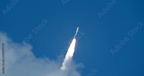 Rare shot of commercial Space Rocket with bright flames and exhaust smoke emerging from clouds into beautiful blue sky. 4K at  120 fps slow motion.