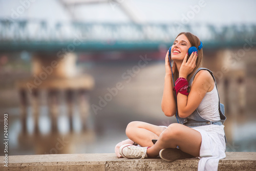 Portrait of smiling young urban woman using smart phone outdoors while waiting for her friends. Listening music.