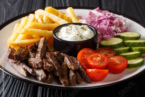 Beef Doner kebab on a plate with french fries, salad and sauce close-up on a table. Horizontal