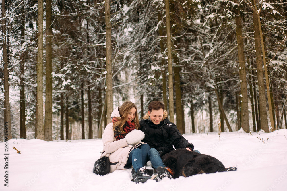 Obraz premium young couple having fun in winter park with their dog. Hugging young couple in love walking with dog outdoors in snowy winter
