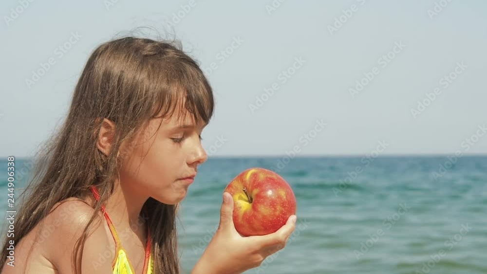 Teenage girl having snack on the seaside. Cute little girl eats an apple on the beach against the background of the sea. Teenage girl having snack on the seaside. Cute little girl eats an apple on the beach against the background of the sea.