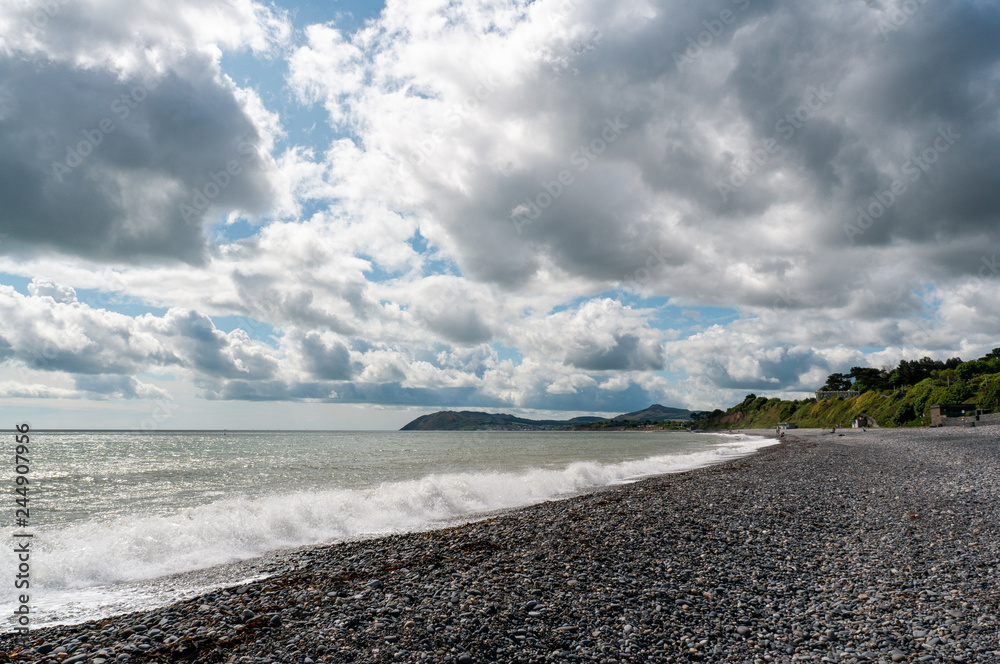 Dramatic pebble beach landscape with storm clouds gathering and white surf waves on the Irish East Coast. Seascape in Killiney, Dublin , Ireland.