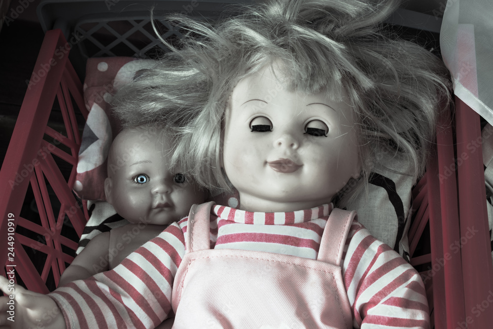 Creepy dolls. Baby doll with one bright eye is lying behind a sleeping girl doll Stock Photo Adobe Stock