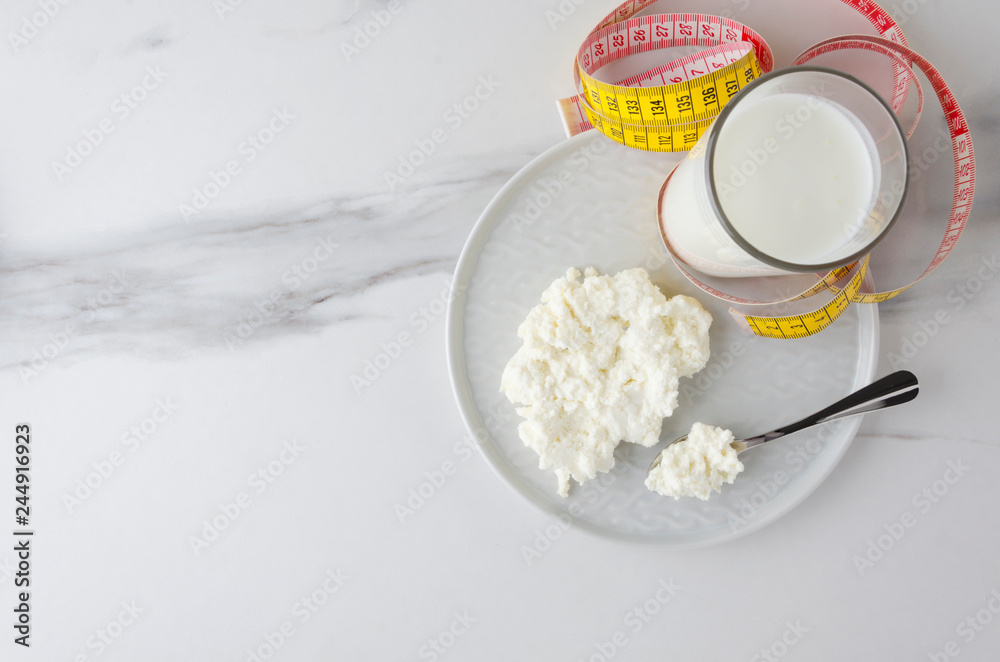 Top view of meal ingredients for milky diet,loss weight.Spoon with cottage cheese and plate,glass with milky product,measuring tape Top view of meal ingredients for milky diet,loss weight.Spoon with cottage cheese and plate,glass with milky product,measuring tape
