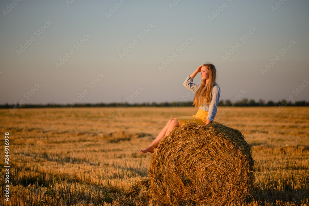 The beautiful young girl in the field about harvesting time against the background of sheaves with straw The beautiful young girl in the field about harvesting time against the background of sheaves with straw