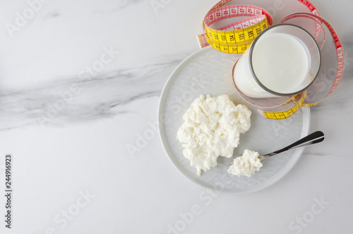 Top view of meal ingredients for milky diet,loss weight.Spoon with cottage cheese and plate,glass with milky product,measuring tape