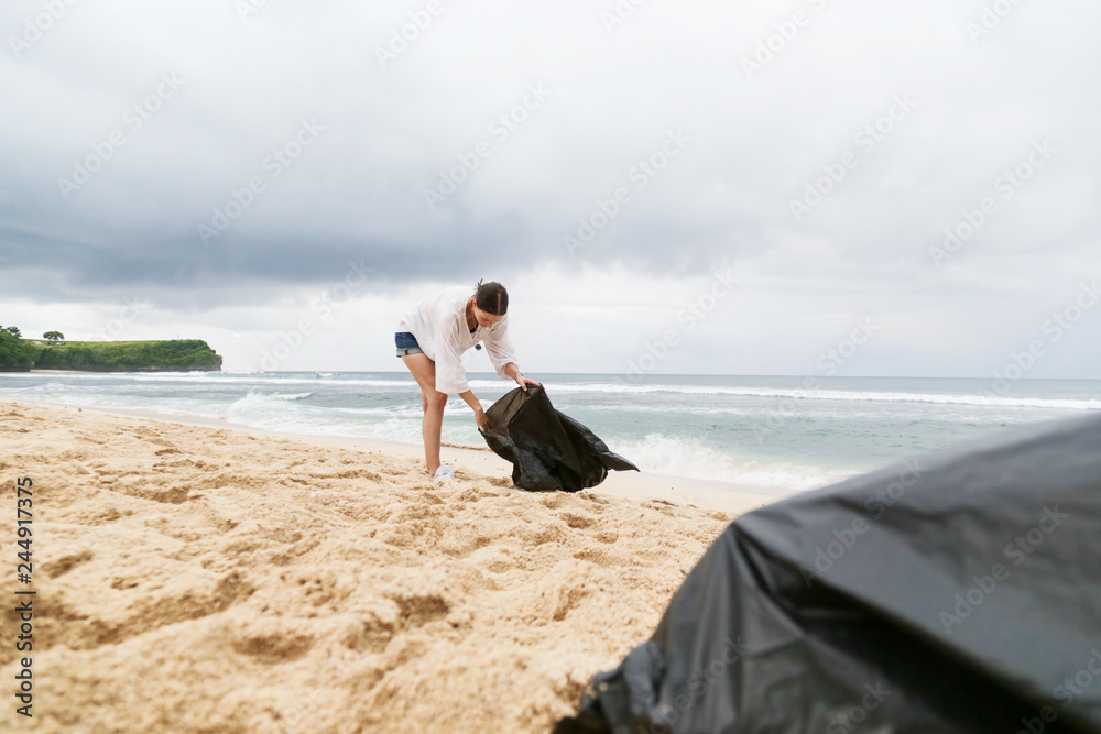 Volunteer woman collecting trash on the beach. Trash-free seas concept. Single-use plastic is a human addiction that is destroying our planet Volunteer woman collecting trash on the beach. Trash-free seas concept. Single-use plastic is a human addiction that is destroying our planet