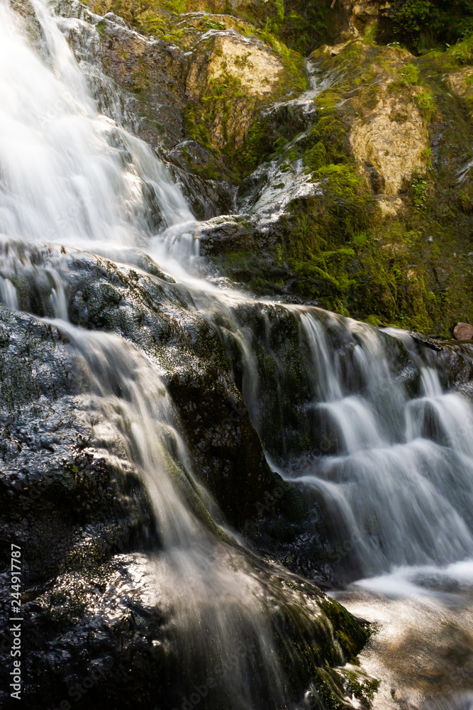 Scenic waterfall on mountain river in summer forest. Travel along river.