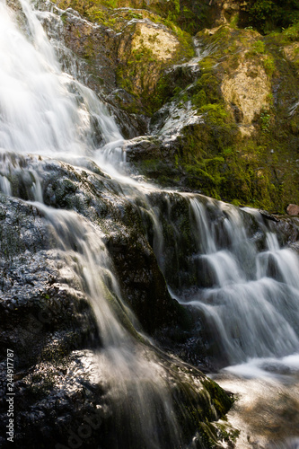 Scenic waterfall on mountain river in summer forest. Travel along river.