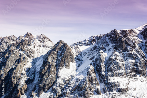 Dawn or sunset in mountains in winter. Mountain range under pink clouds. Rocks are covered with snow and purple sky.