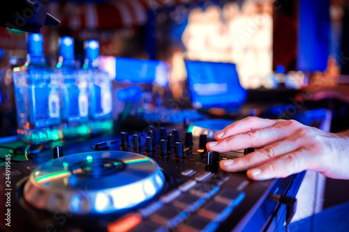 DJ with headphones at night club party under the blue light and people crowd in background