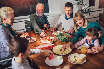 Multi generation family enjoying meal around table at home
