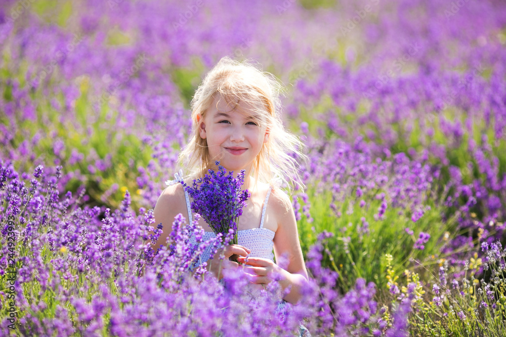 Blonde girl in the colour dress sitting on the field o lavander with a small bouqet in her hands Blonde girl in the colour dress sitting on the field o lavander with a small bouqet in her hands