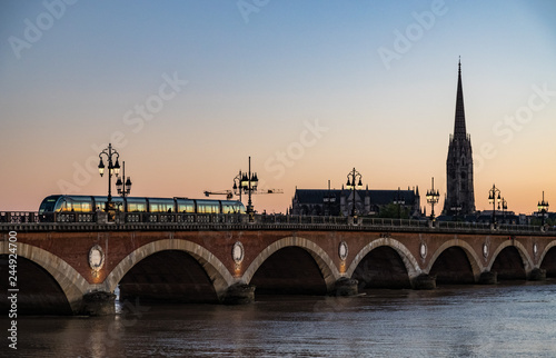 Tram crossing Pont de Pierre bridge in the city of Bordeaux at sunset.