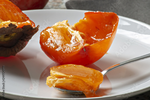 frutto kaki nel piatto tagliato a metà e cucchiaino pieno primo piano photo