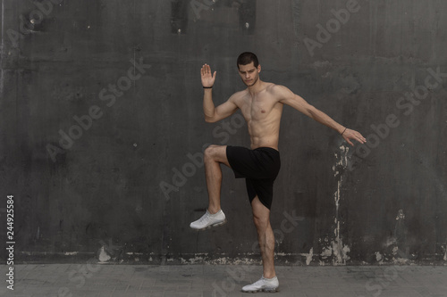 Young athlete man, naked torso, running against a gray wall