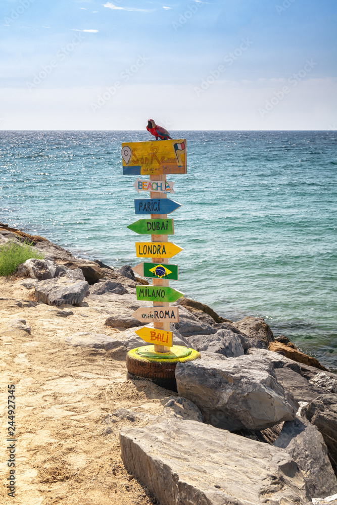 Colorful pole with arrows pointing to place names around the world, on the beach of San Remo