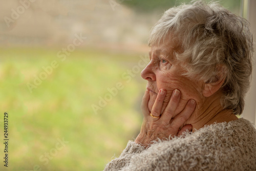 Senior woman looking upset and distressed through a window 